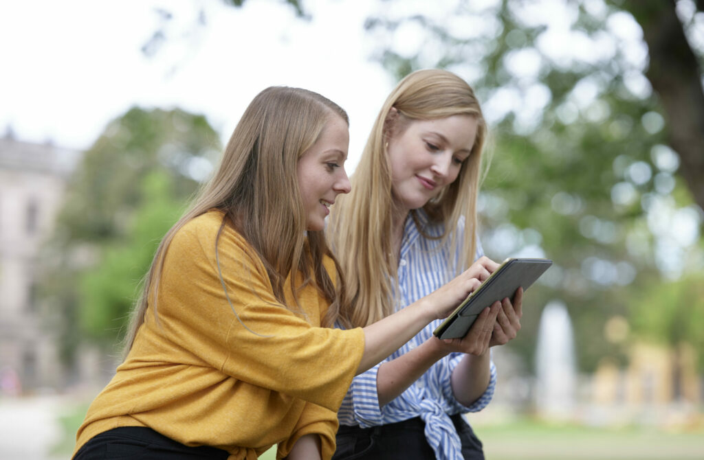 Two students are outside and look at a tablet together.