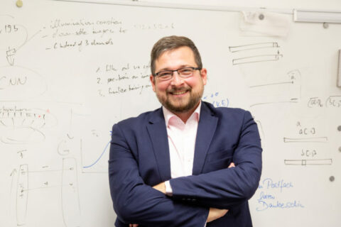 Prof. Dr. Bernhard Kainz is standing in front of a whiteboard. He has his arms crossed and is smiling.